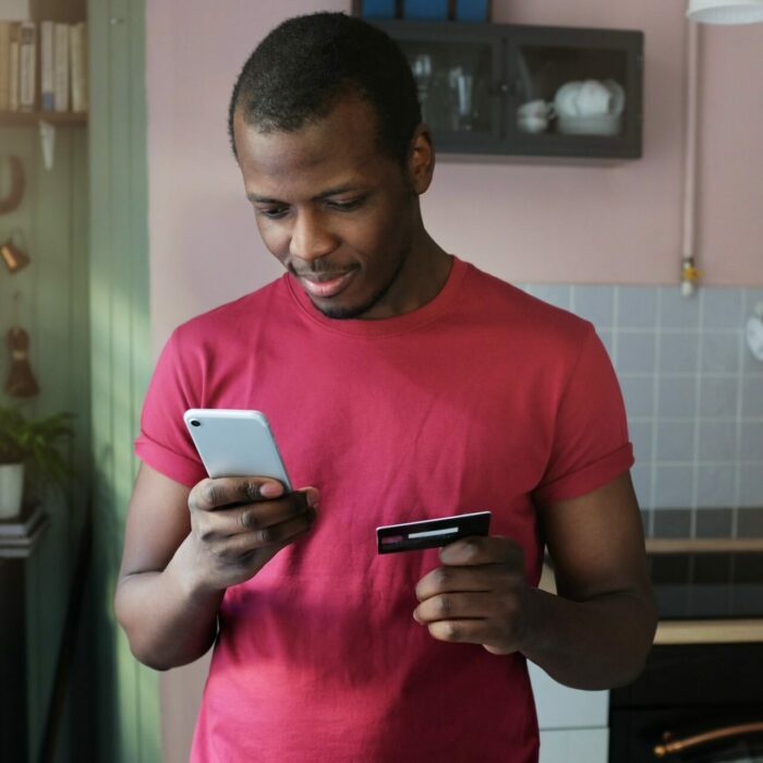 young african american man holds smartphone in one hand and credit card in another 1